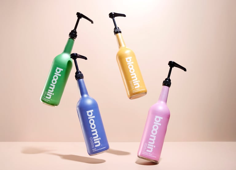 Vibrant product photography of colorful Bloomin pump bottles suspended mid-air against a warm beige