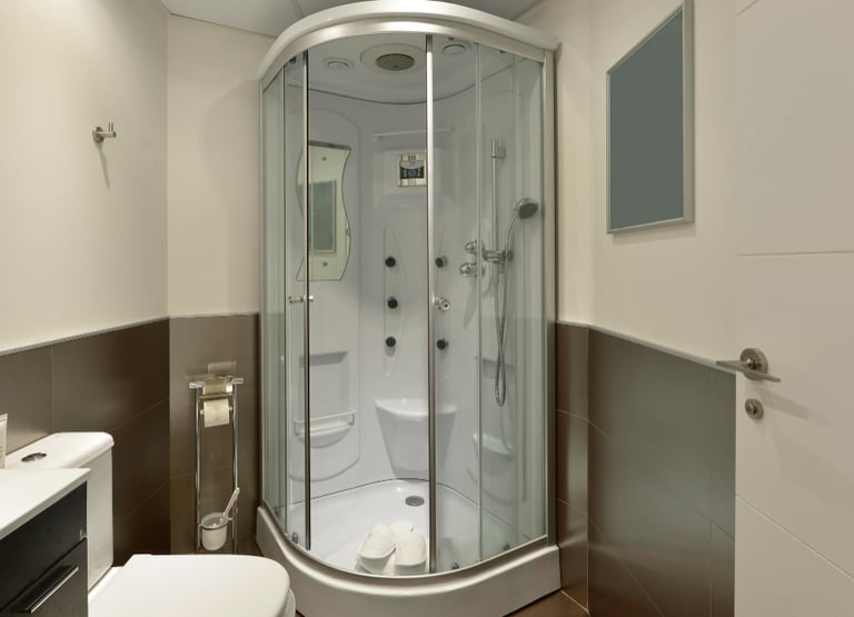 Semi-circular glass shower enclosure with hydromassage panel, sink and toilet