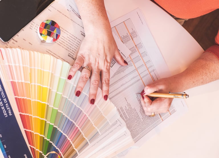 Interior designer choosing paint colors from a fan deck swatch while writing on a technical document.