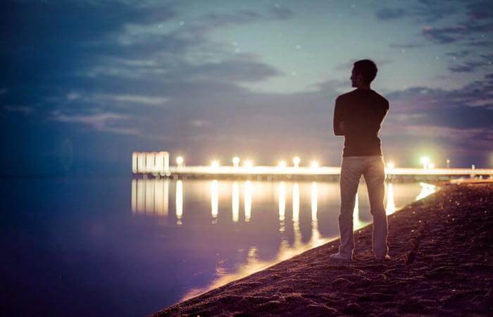 Person standing by water at night, reflecting quietly, symbolizing searching or contemplation.