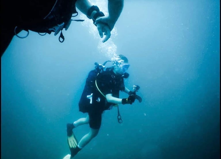 Scuba diver wearing full gear and fins swimming in deep blue ocean water.