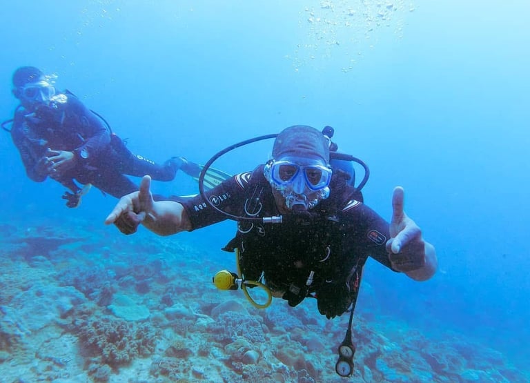 Two scuba divers swim over a colorful coral reef in clear blue tropical ocean water.