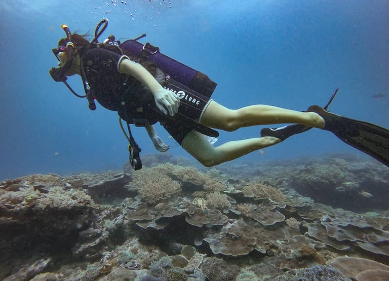 Scuba diver with fins swimming over a vibrant coral reef in clear blue ocean water.