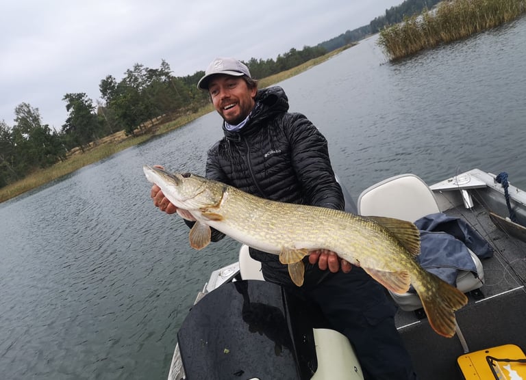 ein Mann ist auf einem Boot; Er ist glücklich, in Schweden einen großen Hecht gefangen zu haben.