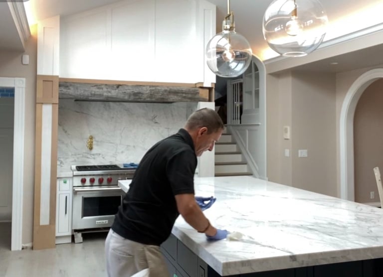 Professional Applicator sealing a white marble kitchen island countertop during a home renovation.