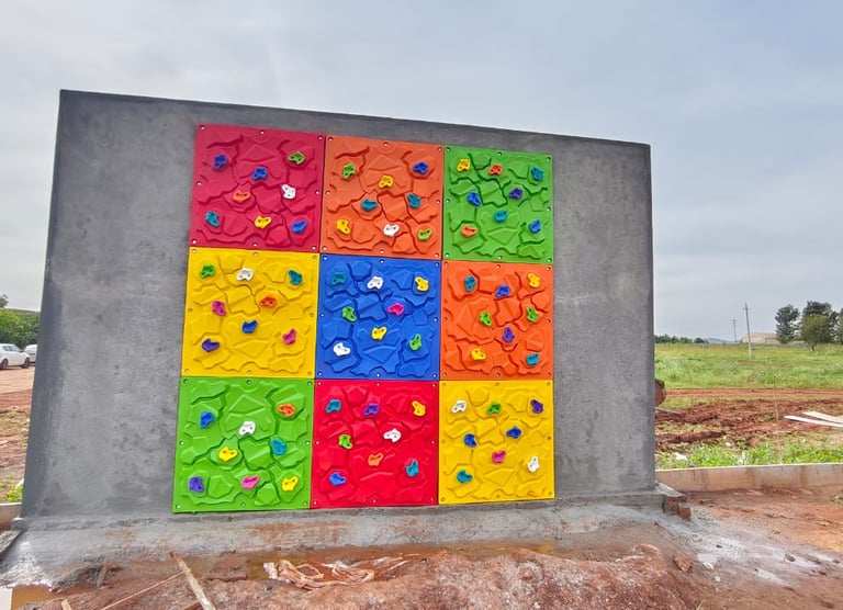 Colorful outdoor rock climbing wall for kids featuring multi-colored hand holds on a concrete structure.