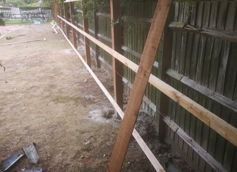 Wooden garden fence construction showing timber rails and posts being installed with a red string line.