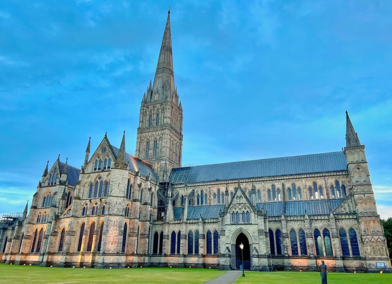 Historic Salisbury Cathedral featuring its iconic tall spire and Gothic architecture under a blue sky.