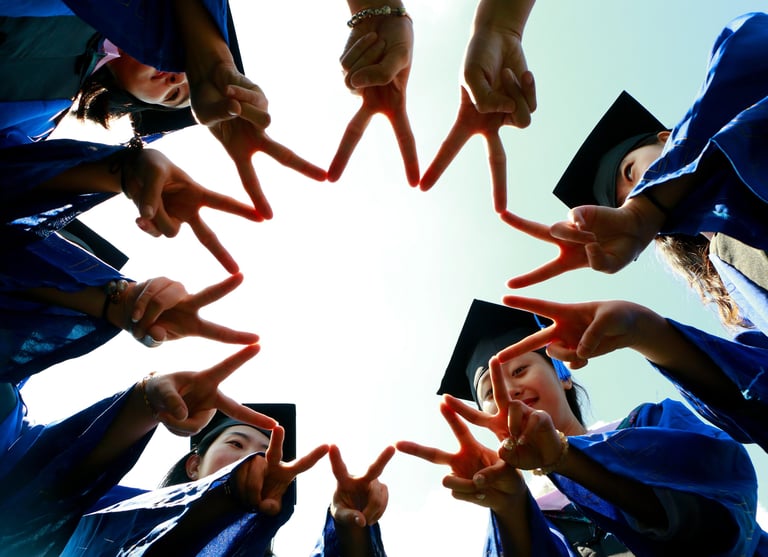 Group of graduates in blue gowns and caps forming a star shape with their fingers while celebrating
