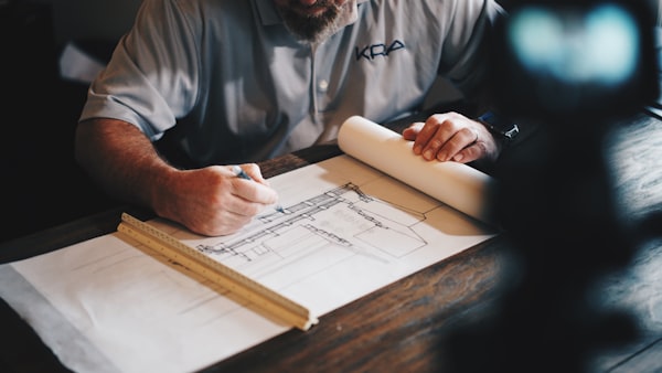 An architect drafting detailed building blueprints and construction plans at a wooden desk.