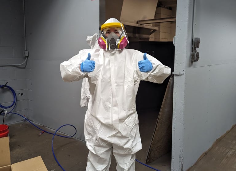 woman wearing protective suit, respirator, gloves, and face shield holding two thumbs up