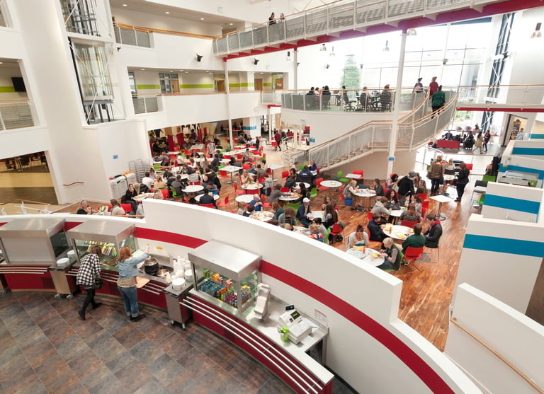 Students dining in a busy multi-level modern university cafeteria and student union hub.
