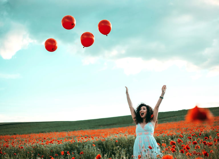a woman in a white dress is standing in a field with red balloons
