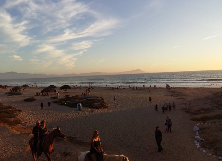 a couple of people riding horses on a beach