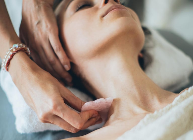 Professional aesthetician performs a facial gua sha massage using a rose quartz stone on a woman's neck.
