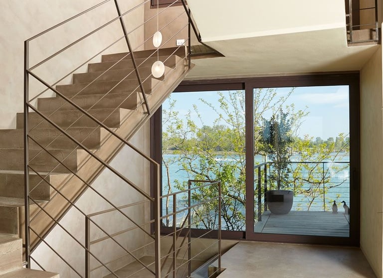 A modern staircase in microcement with metal handrails, offering views of a picturesque lake through