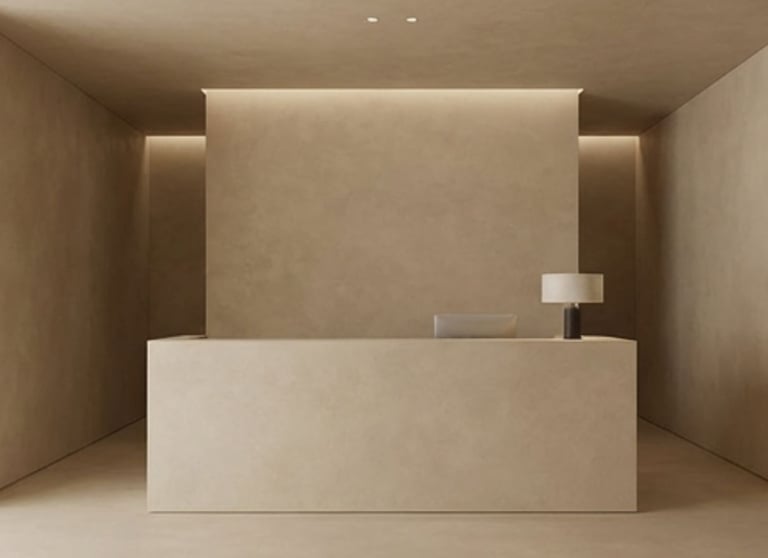 Minimalist reception desk in a modern beige office lobby with warm cove lighting.