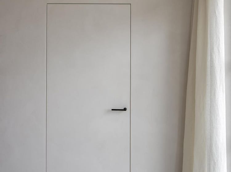 Minimalist white interior door with microcement finish, black handle and stone tile flooring.
