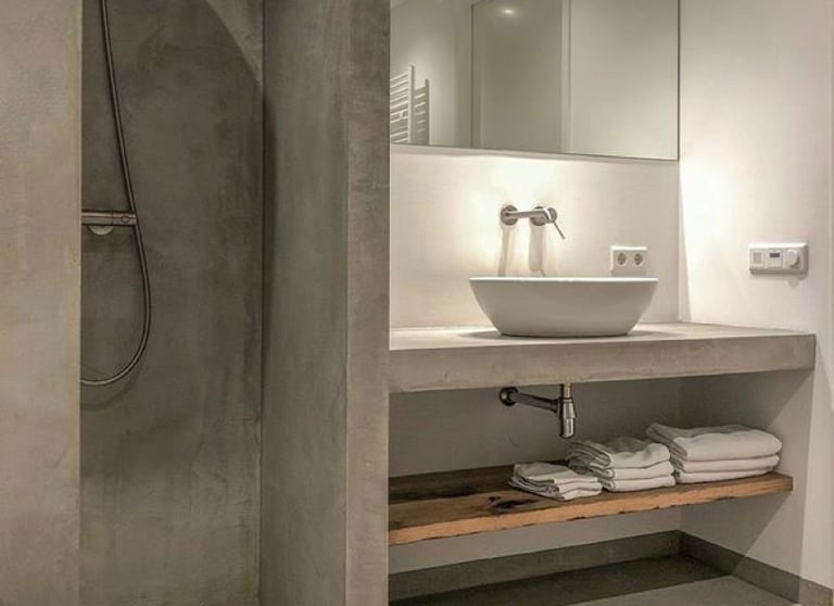 Modern industrial bathroom featuring a microcement walk-in shower and floating concrete vanity with a vessel sink.