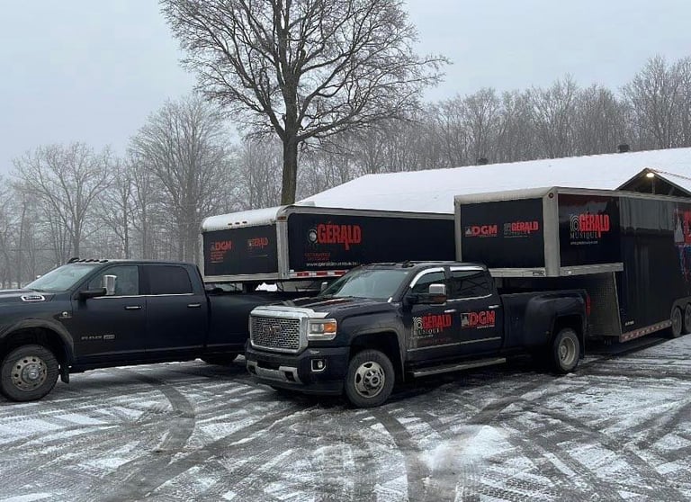 Black Ram and GMC dually trucks towing Gerald Musique trailers in a snowy parking lot.