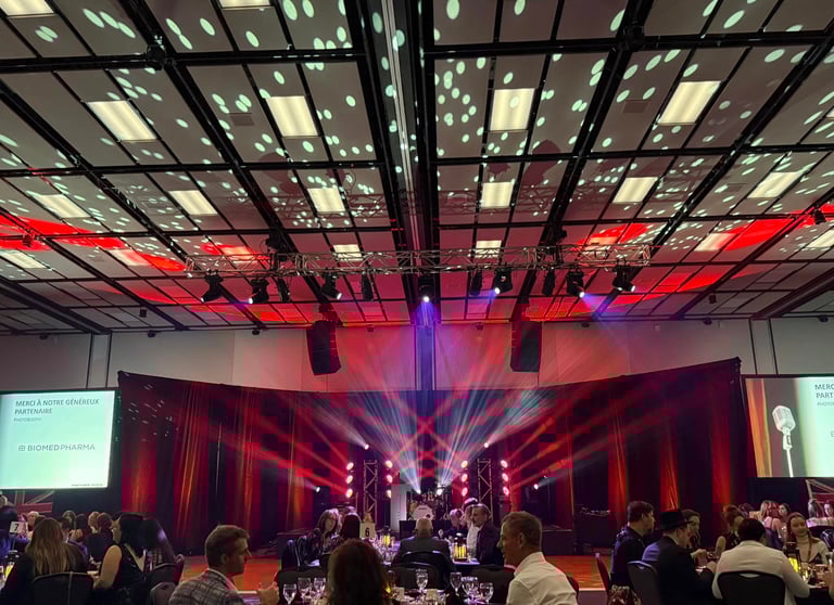 A corporate gala event featuring red stage lighting, spotlights, and guests seated at banquet tables.