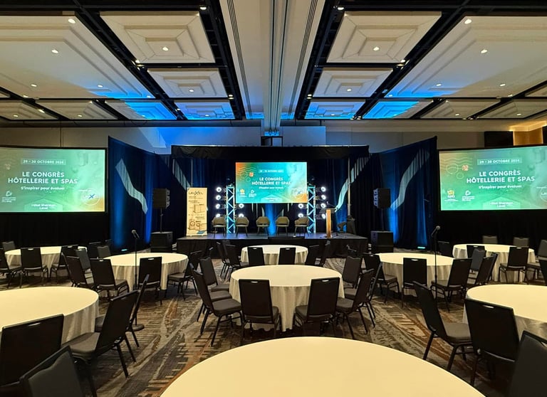 Conference room setup for the "Congrès Hôtellerie et Spas" at the Sheraton Laval, featuring a stage with large screens