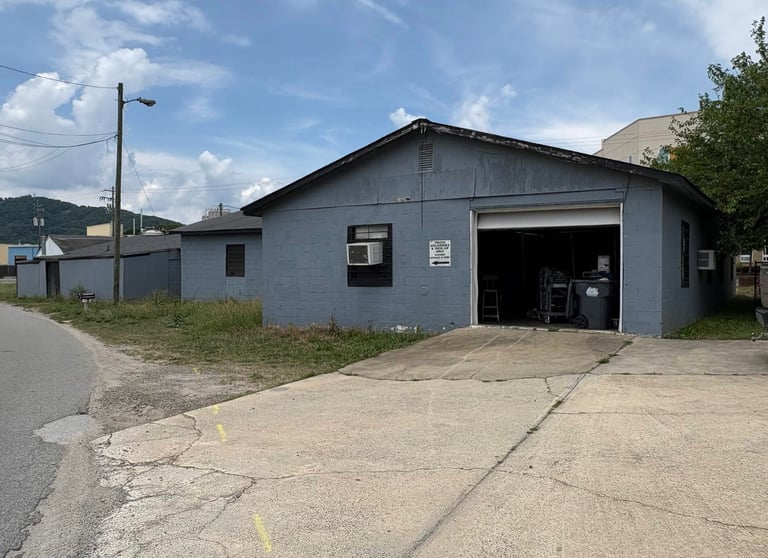 Gray concrete block industrial building with an open garage bay and adjacent driveway.