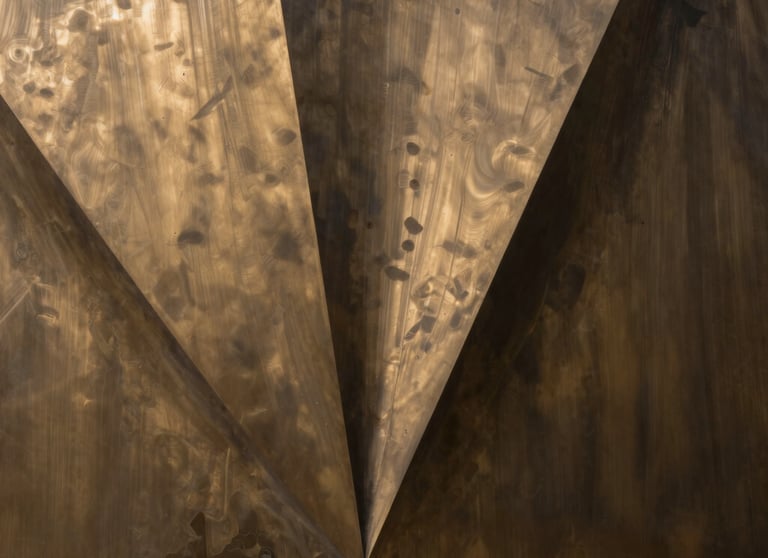Abstract photography of light and shadows on a bronze metal surface, representing creative flair and corporate precision.