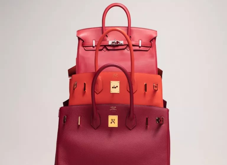 Stacked red and orange luxury Hermes birkin handbags showcasing premium leather craftsmanship.