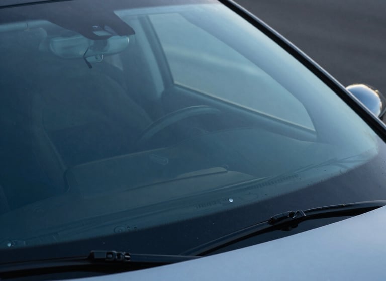 Photography of a modern car parked on a quiet US street, showing the windshield reflecting a clear sky blue horizon, emphasizing safety and clarity, modern efficiency style.