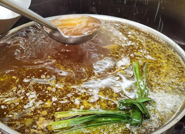 a picture of pho being cooked with a spoon of broth being taken out