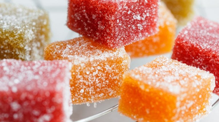 Assorted square fruit jelly candies coated in sparkling sugar crystals on a cooling rack.