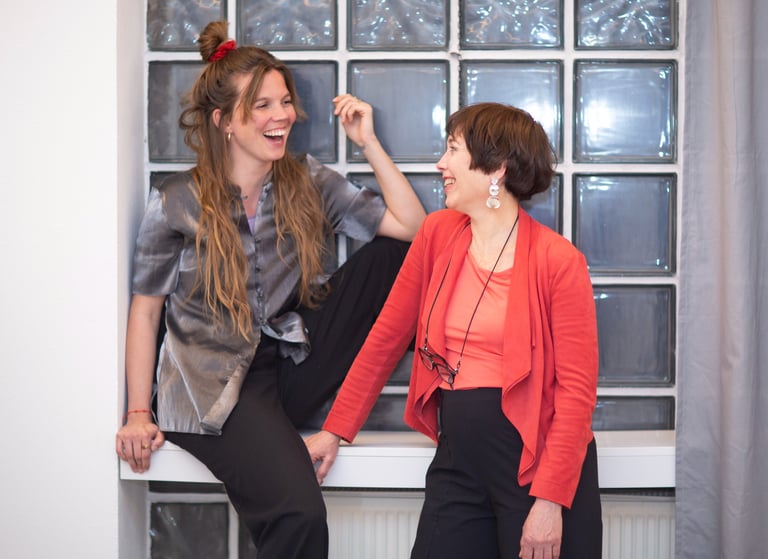 Two smiling female public speaking trainers in Berlin, looking at each other