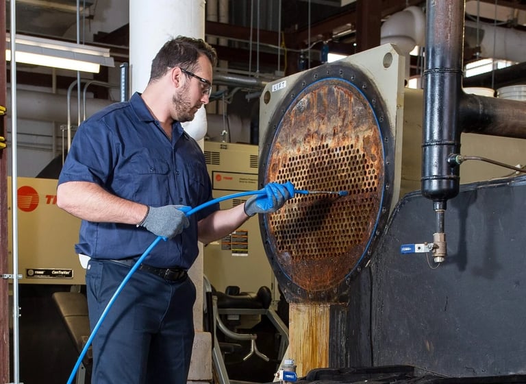 An HVAC technician performs maintenance by cleaning industrial chiller condenser tubes.