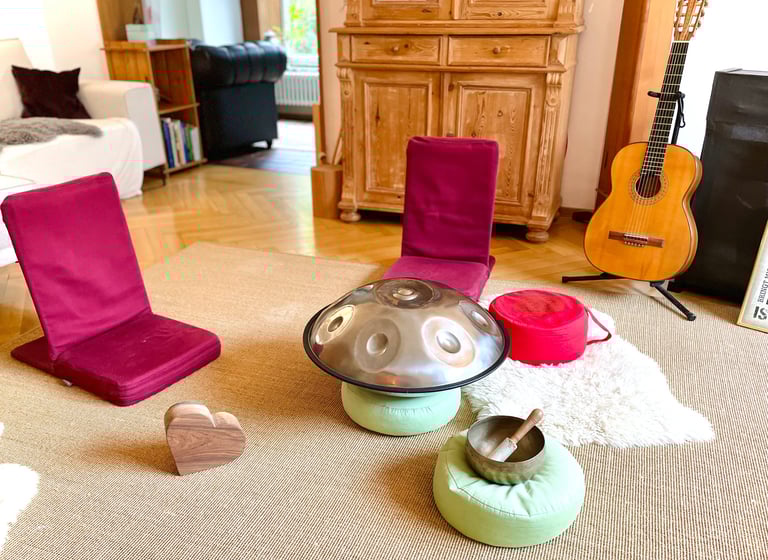 ein heller Raum mit Bodensitzern, einer Handpan und Meditationskissen