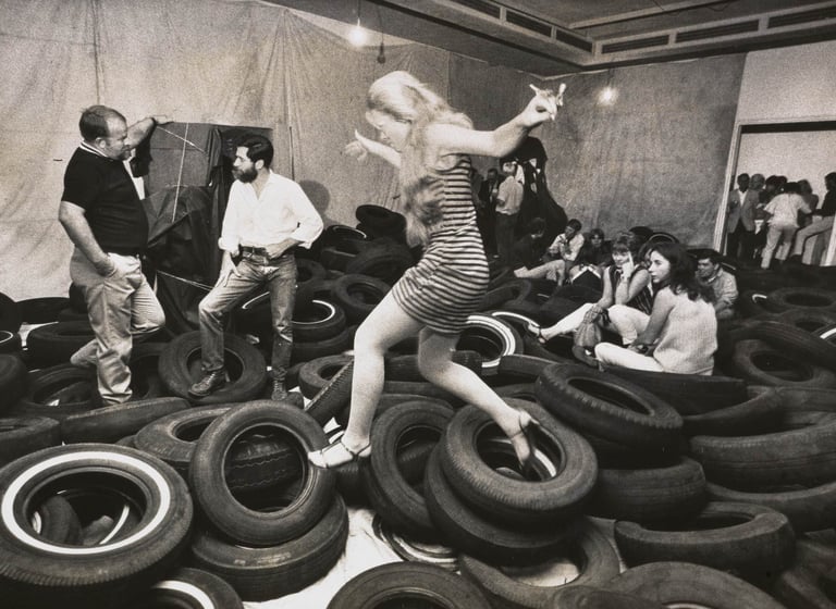 Participantes explorando pilhas de pneus pretos na instalação ‘Yard’ de Allan Kaprow, reconfigurando