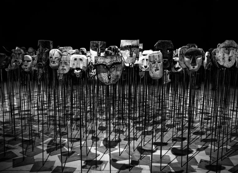 Foto em preto e branco de diversas máscaras tribais em varas.