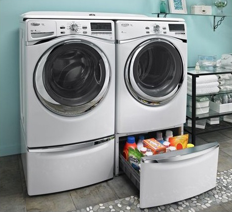 Front-loading washer and dryer in a laundry room with a storage drawer containing detergent and cleaning supplies underneath.