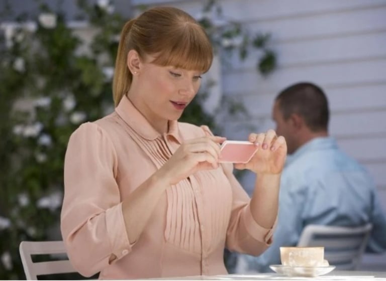 a woman in a pink shirt is holding a cell phone