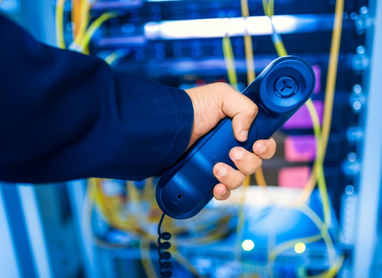 Person holding a phone behind a network rack, representing IT support and remote troubleshooting services