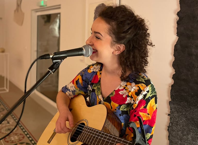 Une femme musicienne qui joue de la guitare et qui chante dans un micro sur pied