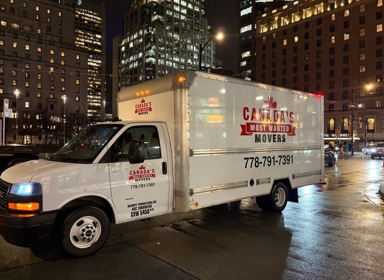 Canada’s Most Wanted Movers box truck operating in downtown Vancouver on a rainy evening.