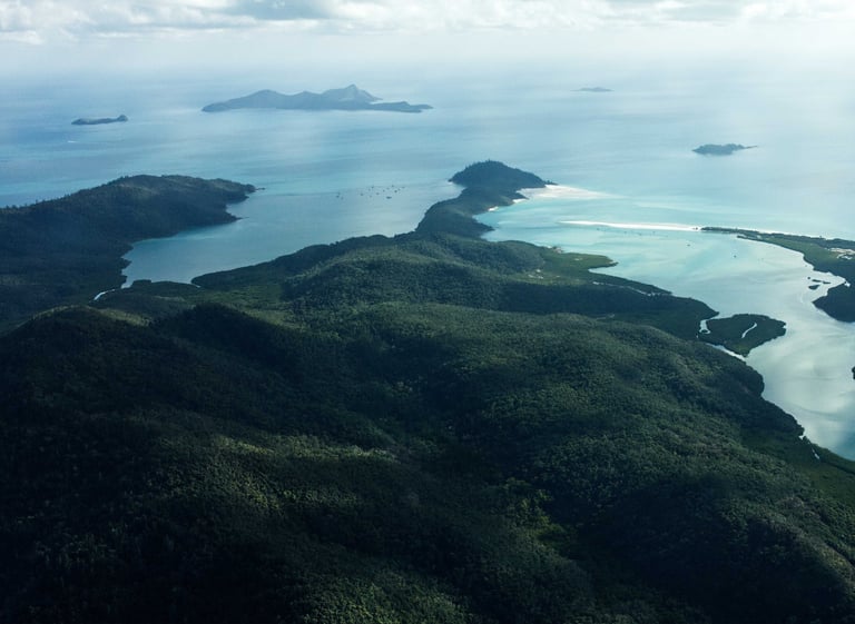 Aerial view of lush green Whitsunday Islands with turquoise water and white sand beaches.