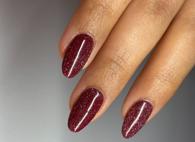Image of perfectly manicured hands with burgundy nails with sparkles in them