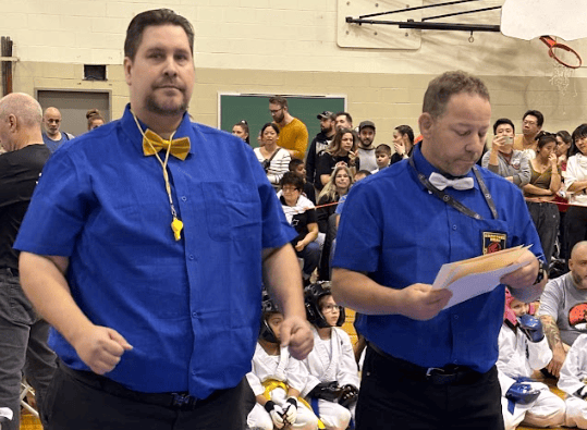 two men standing on a blue mat with a man in a blue shirt