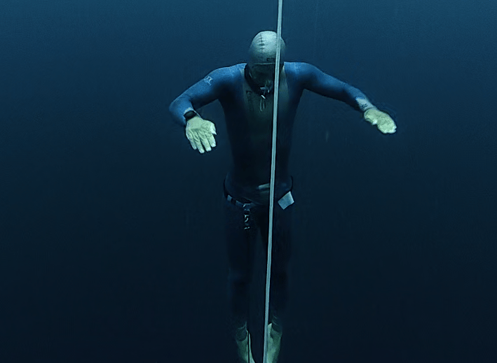 A dark blue picture of a freediver ascending on the line in no-fins technique