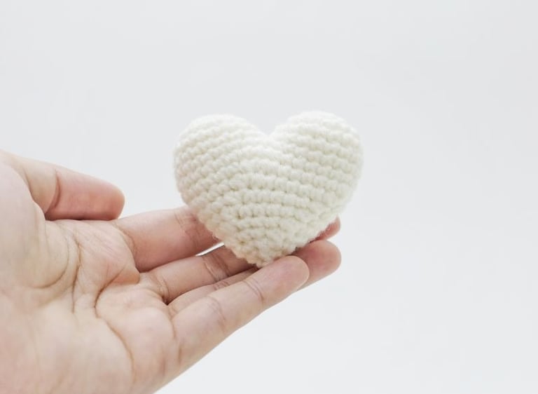 Mano sosteniendo un corazón de crochet color blanco