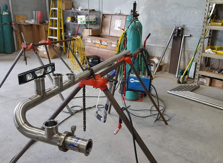 Custom stainless steel pipefitting on a welding stand in an industrial workshop.