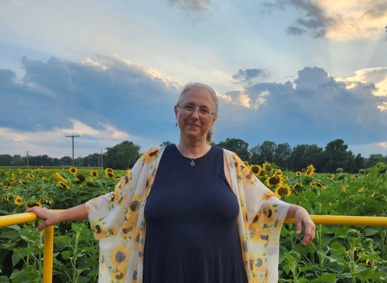 Woman leaning against a fence in a sunflower field.