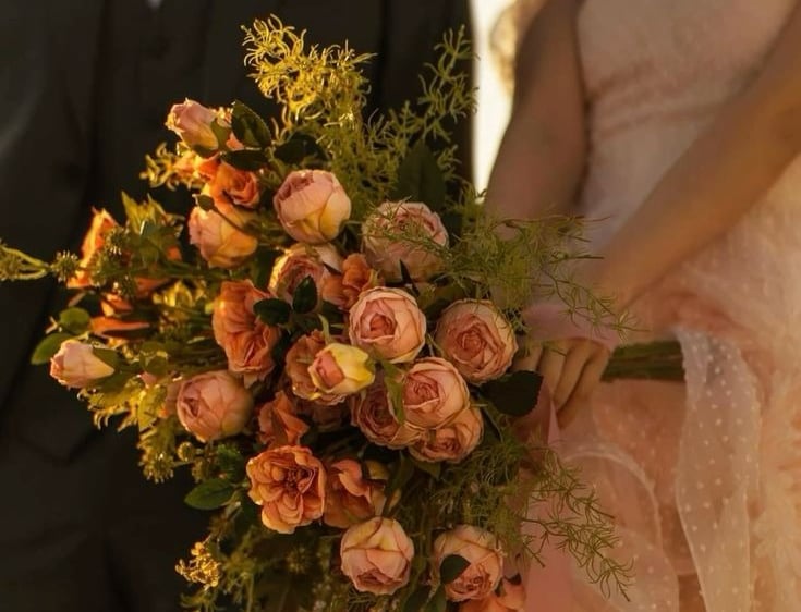 Novia con ramo de rosas en tonos durazno y verde.